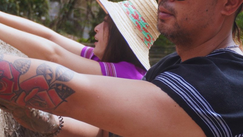 Two people in hats reaching towards something outdoors.