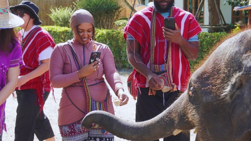 People in colorful attire interact with an elephant at an outdoor park.