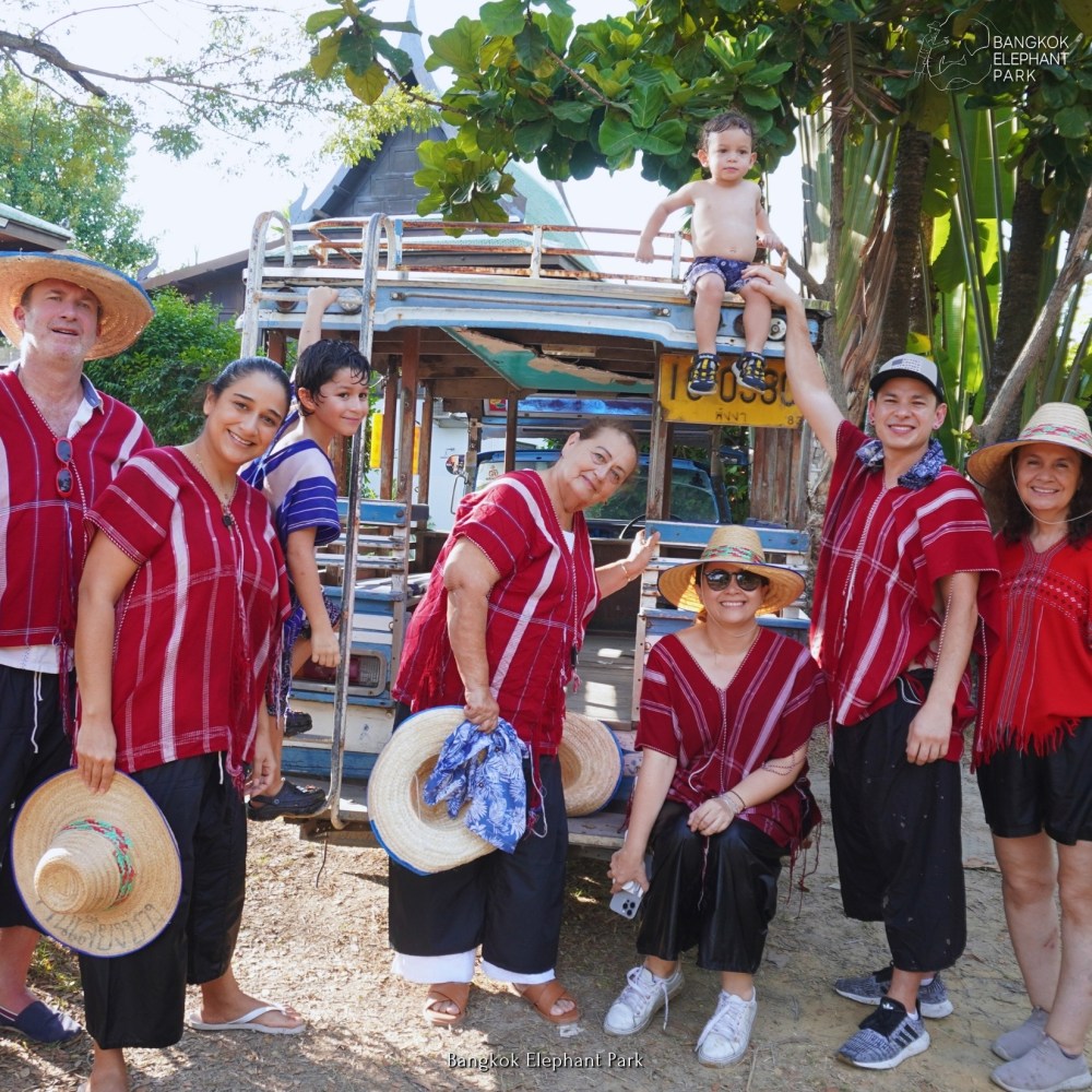 Group of people in red shirts and straw hats posing with a child on a vehicle at Bangkok Elephant Park.
