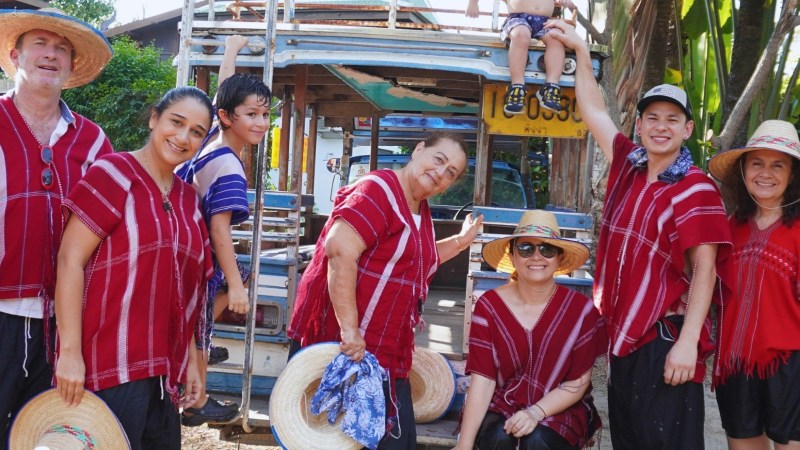 Group of people in red shirts and straw hats posing with a child on a vehicle at Bangkok Elephant Park.