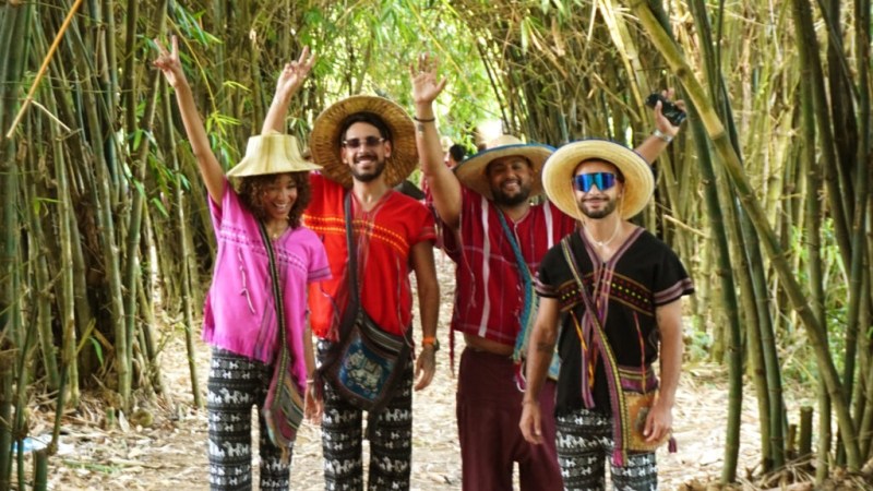 Four people in colorful clothing and hats smiling in a bamboo forest.