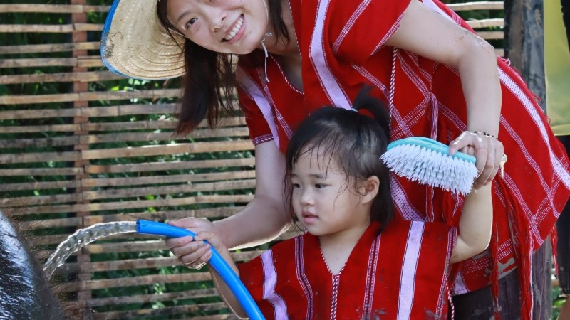 Woman and child in red outfits washing an elephant with a hose and brush.