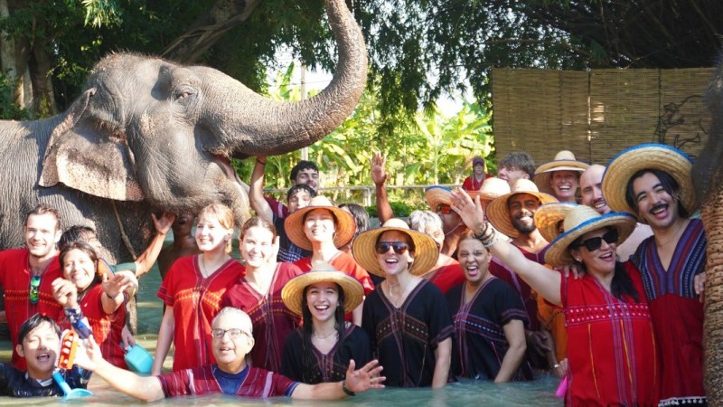 Group of people with elephants in water, wearing straw hats.