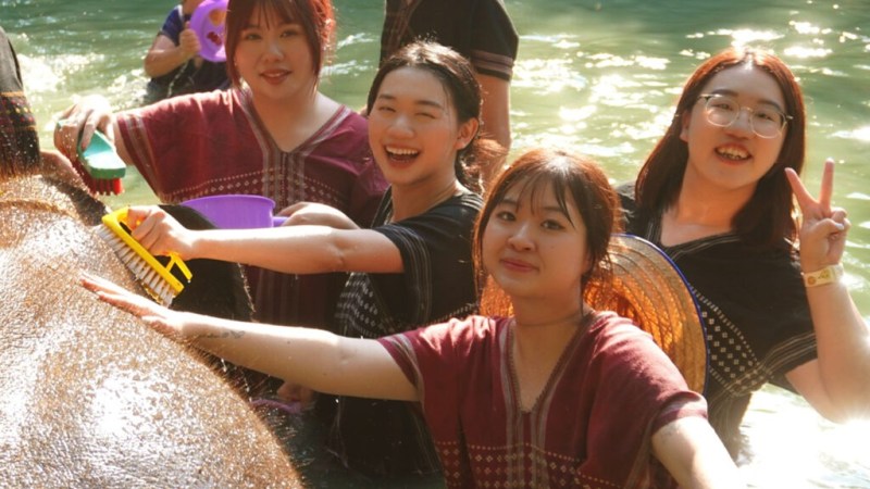 Group of people washing an elephant in a river wearing traditional clothing and smiling.